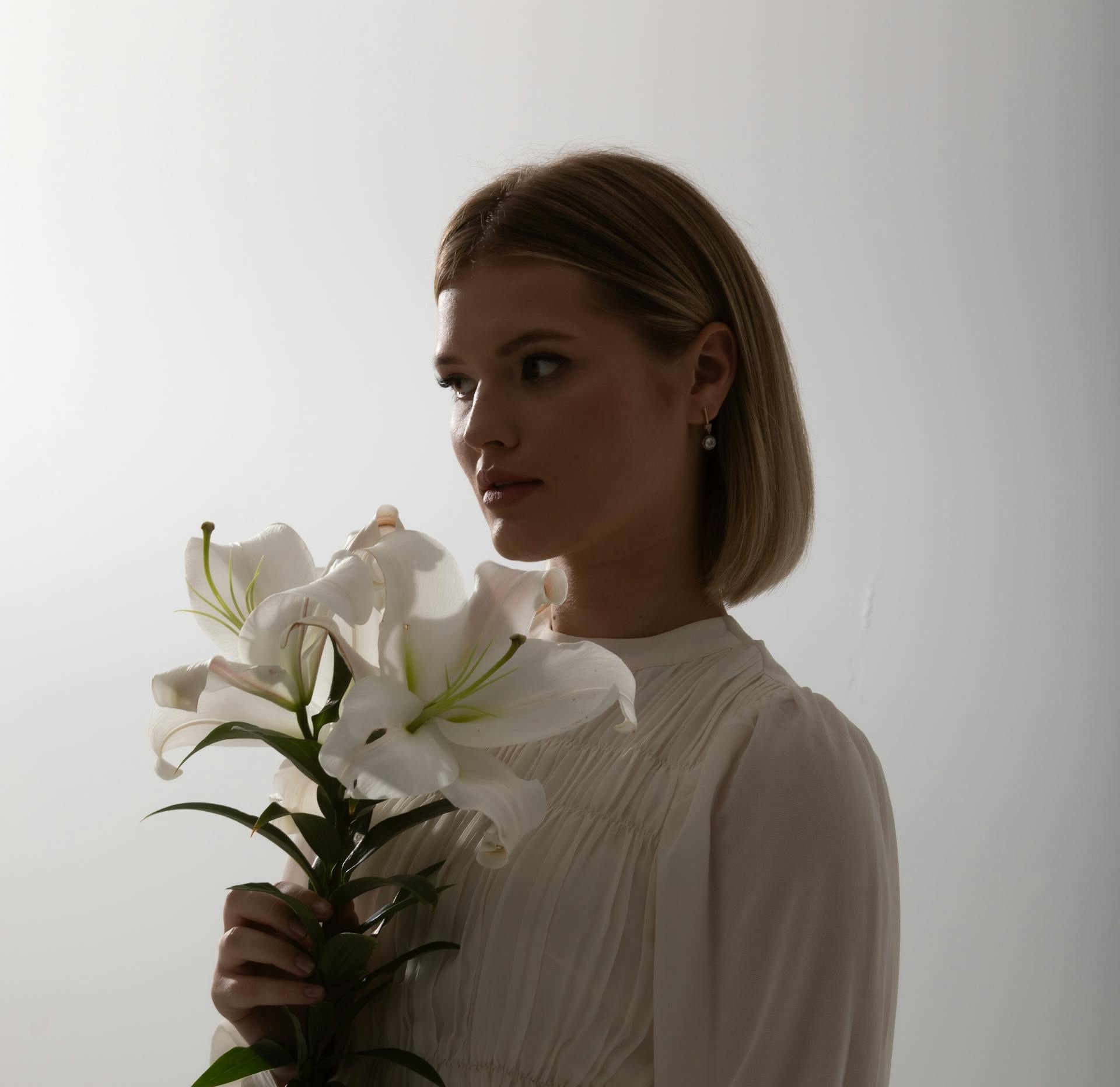 Woman holding a stem of white lilies, several of them open